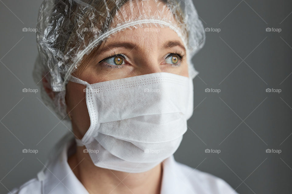 Doctor with face covered with mask. Portrait of young woman wearing the uniform, cap and mask to avoid virus infection and to prevent the spread of disease. Real people, authentic situations