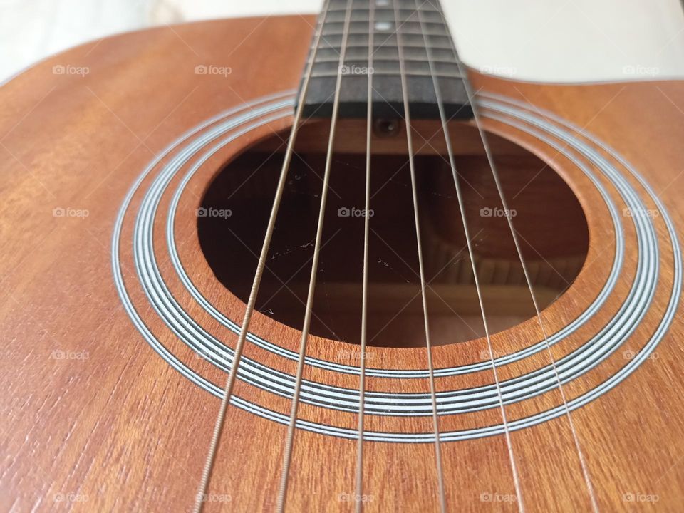 An acoustic guitar is a type of guitar where the sound produced comes from the vibration of the guitar strings that are channeled through the saddle and bridge where the strings are attached into the sound chamber