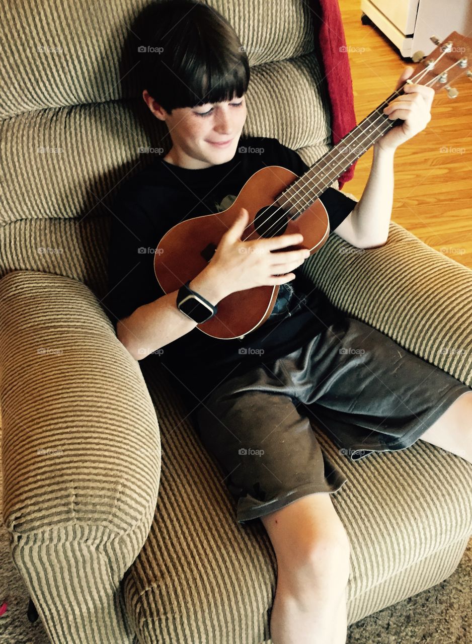 Young boy playing a ukelele in chair.