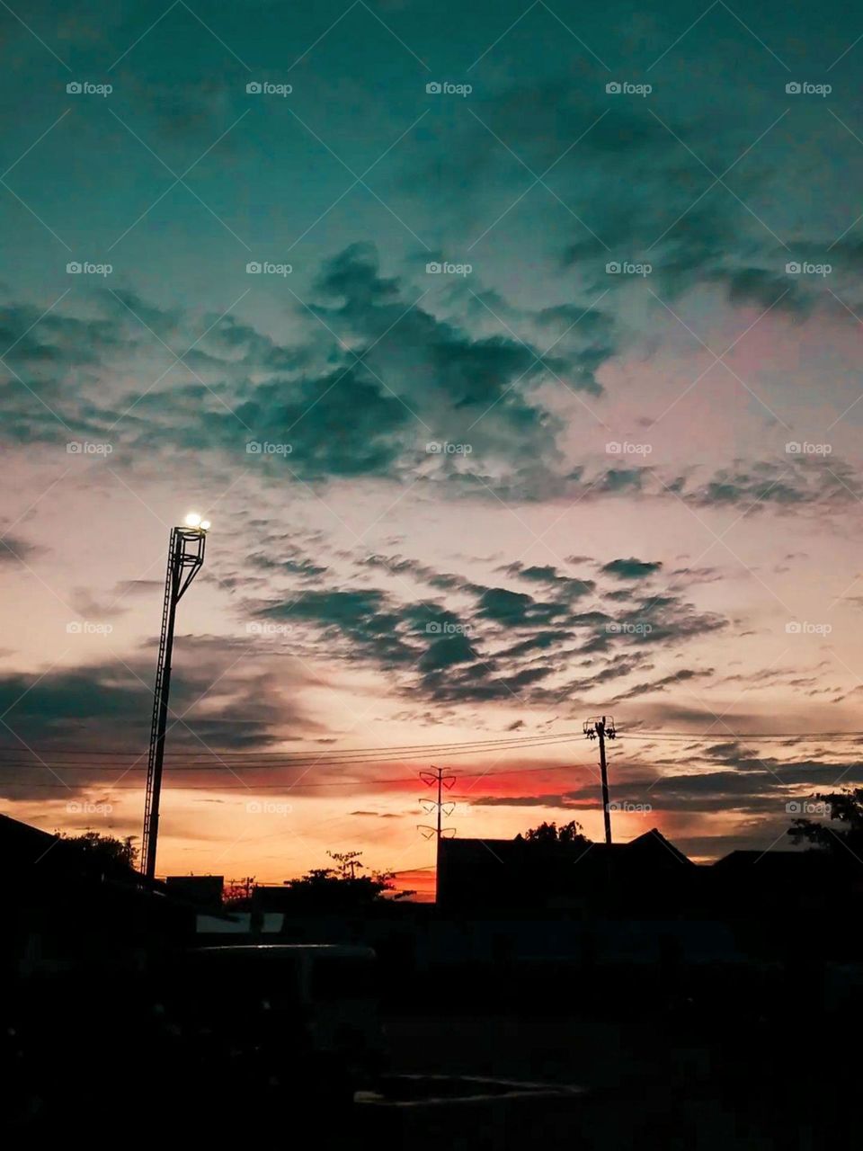 Portrait of a sunset scene with a colorful sky, silhouettes of lampposts and buildings in the foreground