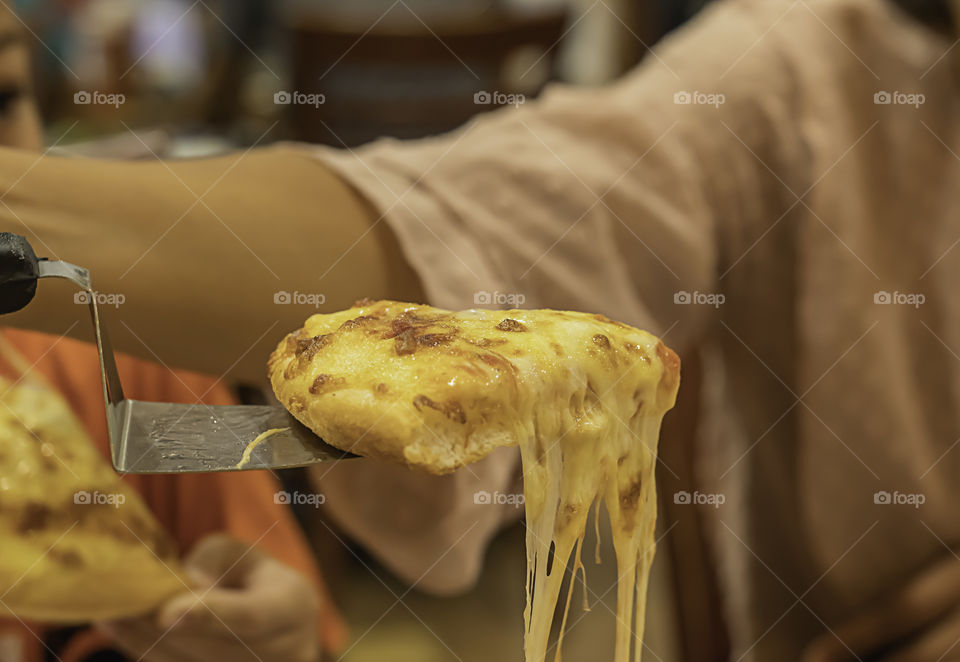 The hand holding Pizza with ham and cheese in spoon from the tray wood.