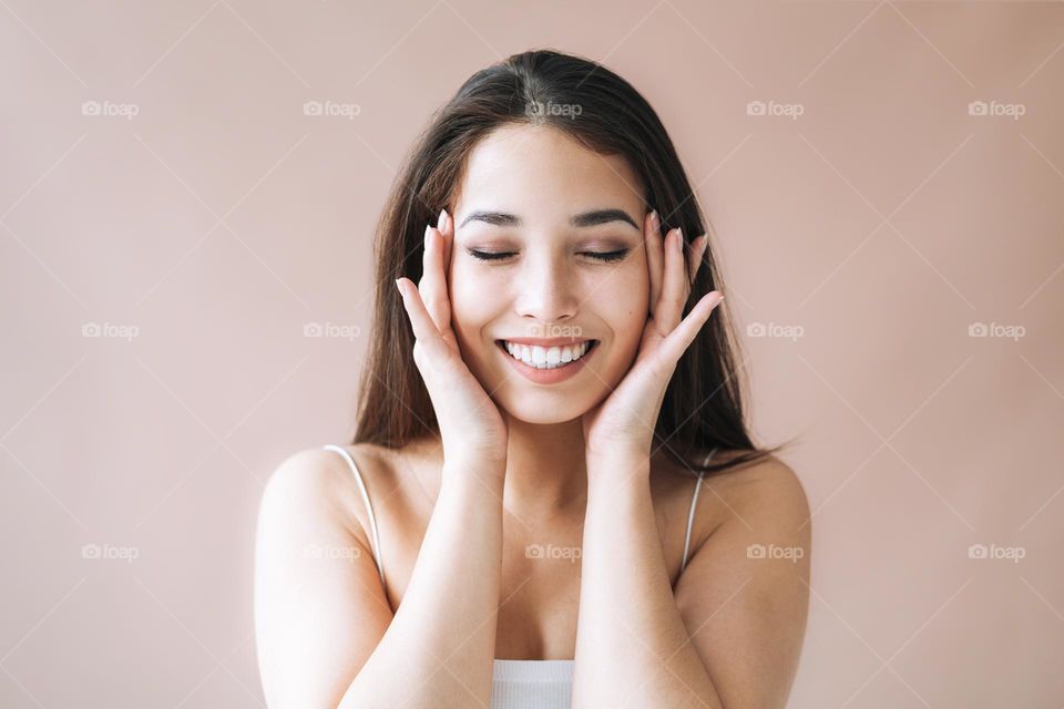 Beauty portrait of young asian woman with healthy dark long hair in top on beige background