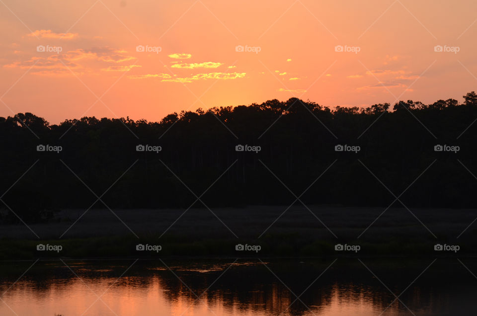 Morning skies are illuminated with a peach hue as the sun comes to ascension during a sunrise rising above the Vernon river marsh in Savannah, Georgia.