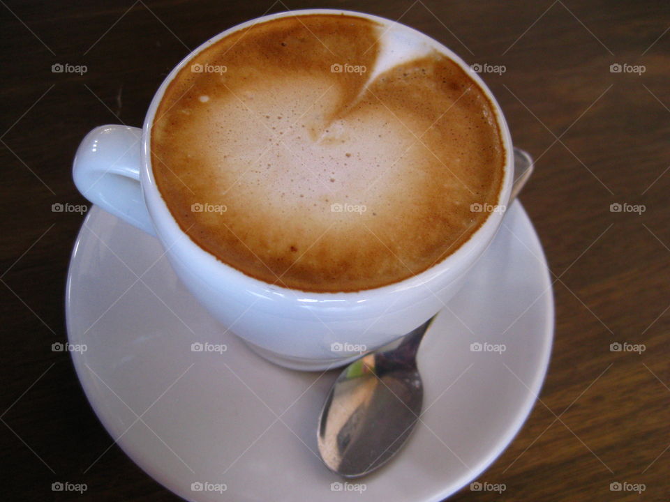 Cappuccino . A cup of cappuccino on a saucer with a spoon. Taken in Oakland, California.