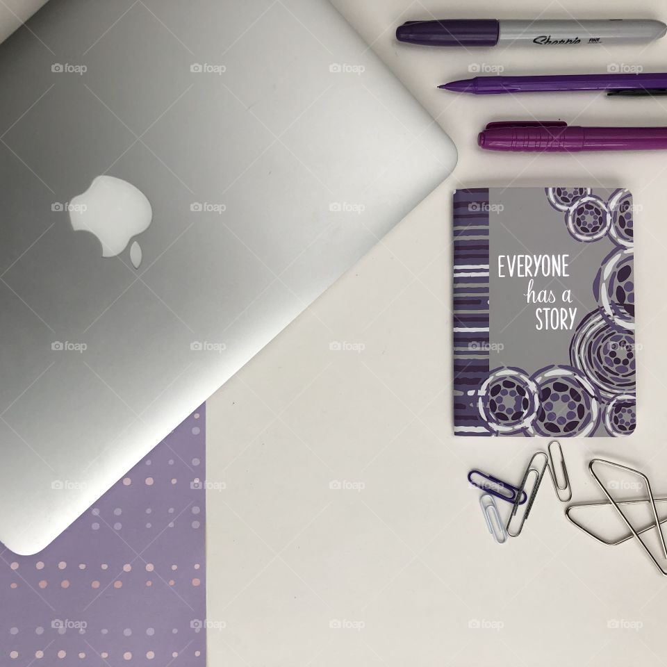 From above flat lay of purple office supplies with a laptop and a notebook with a motivational saying.