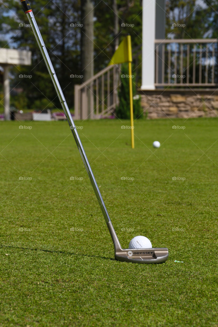 A golfer putts a ball on the green towards a yellow flag