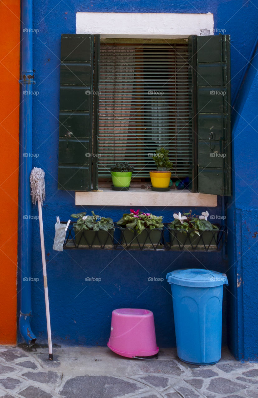 A mop and bucket next to a window of a blue house. Burano, Italy. 