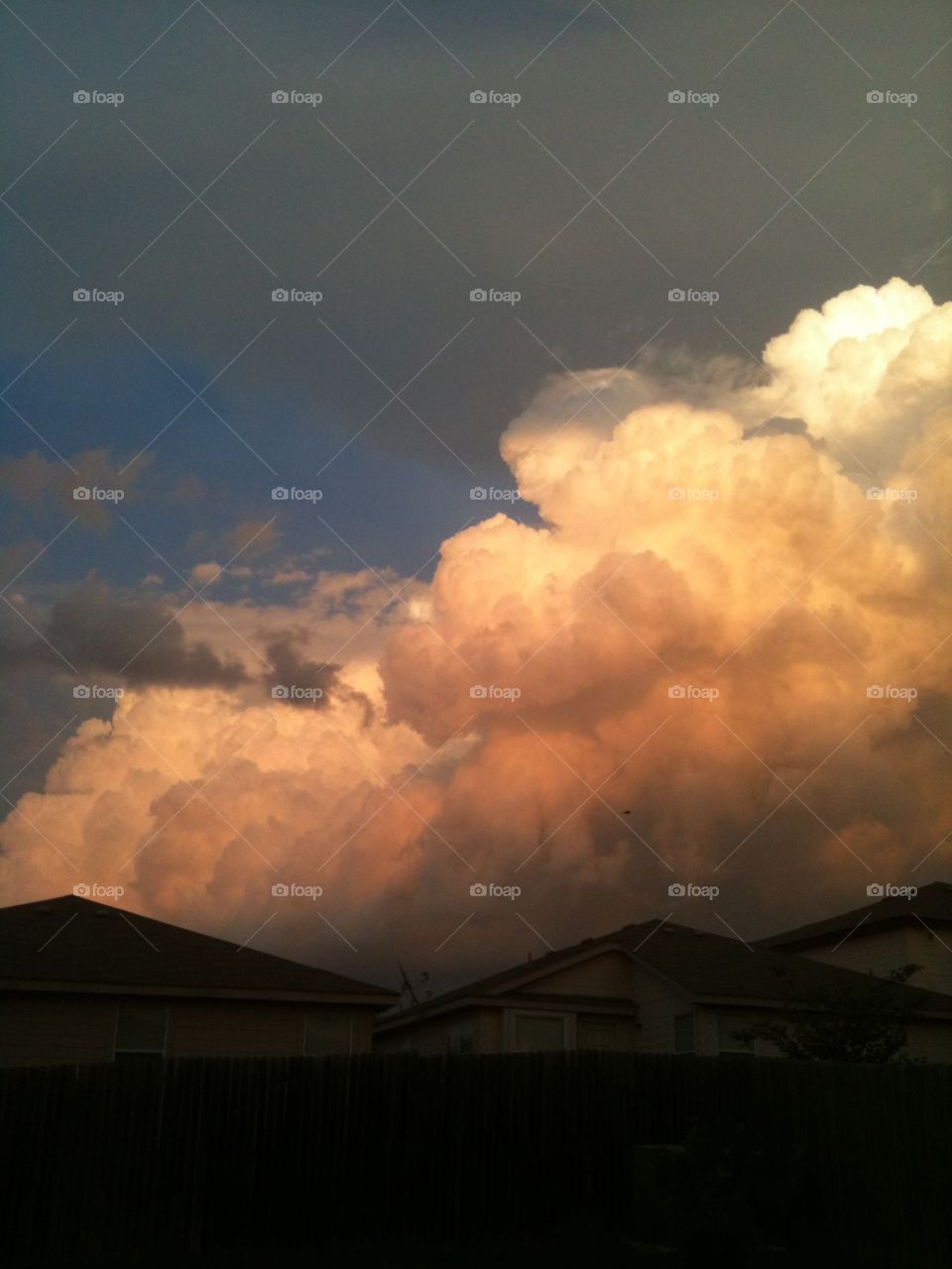 Large storm clouds over houses, clouds lit by sunlight, white thunderhead clouds, rain clouds