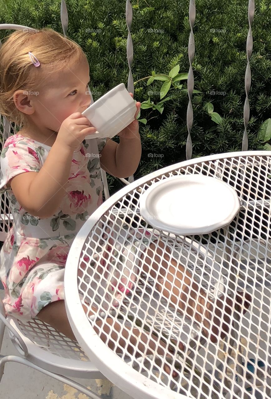 Toddler girl sipping tea at metal table outside