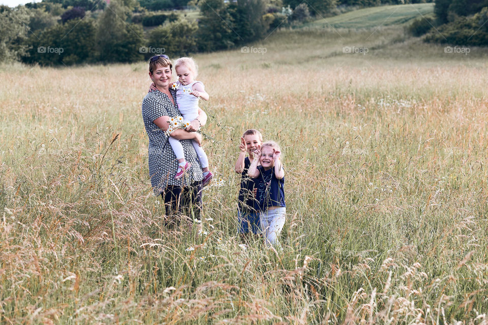 Mother spending time with children on a meadow, close to nature. Woman and kids standing in a grass. Happy kids making faces. Candid people, real moments, authentic situations