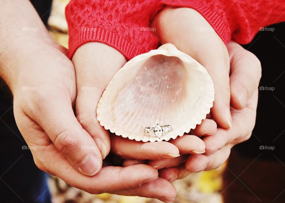 Close-up of couple's hand holding ring in seashell