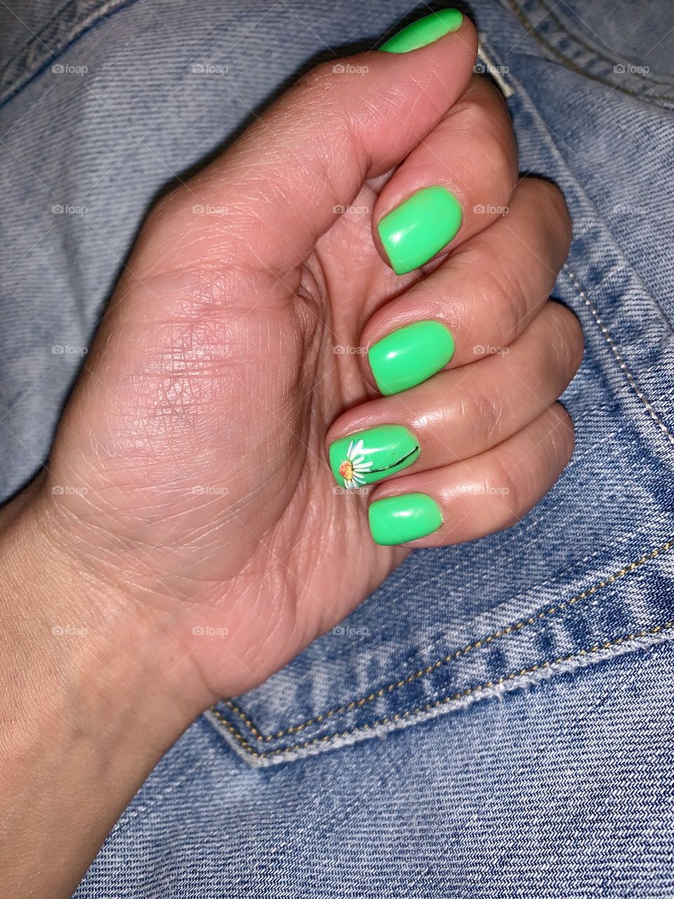 hand with bright green manicure on a denim background