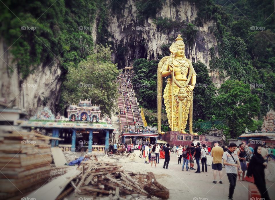 A massive golden statue stands at the bottom of stairs that lead into a huge cave