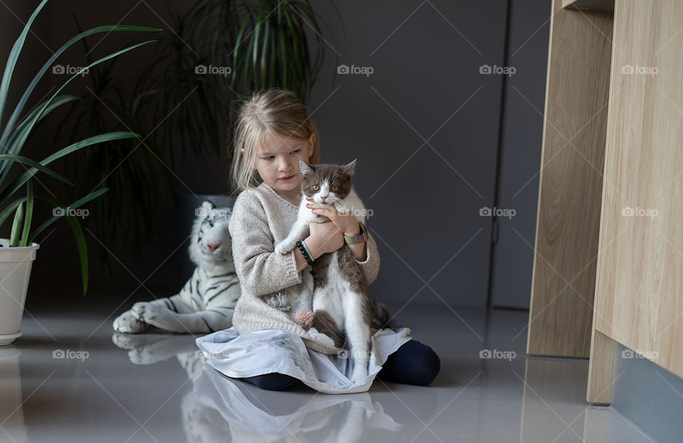 Little girl playing with cat on the floor at home
