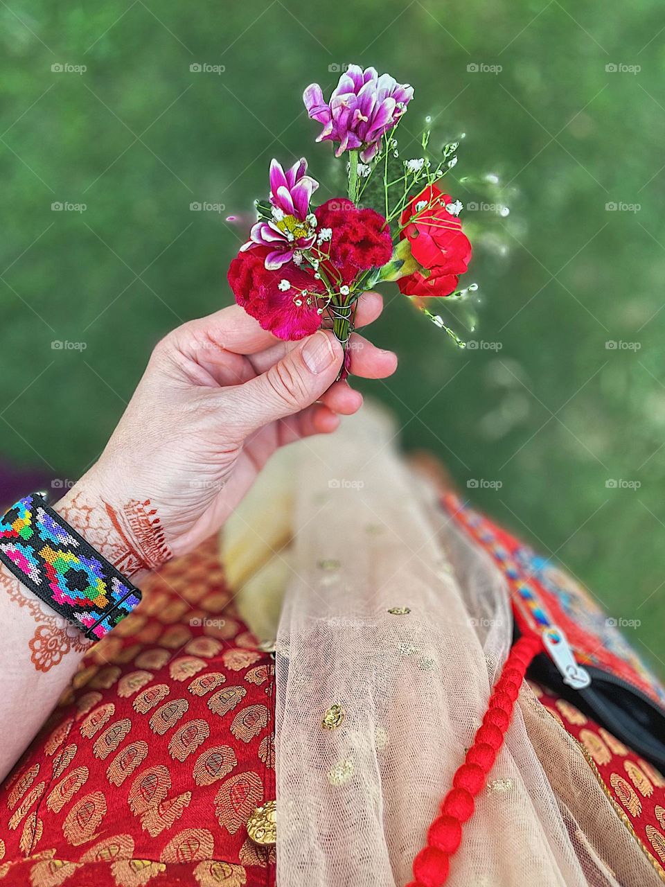 Woman holding small flower bouquet, woman at Indian wedding, celebrating Indian wedding, flowers at a wedding, woman’s hand holding flowers 