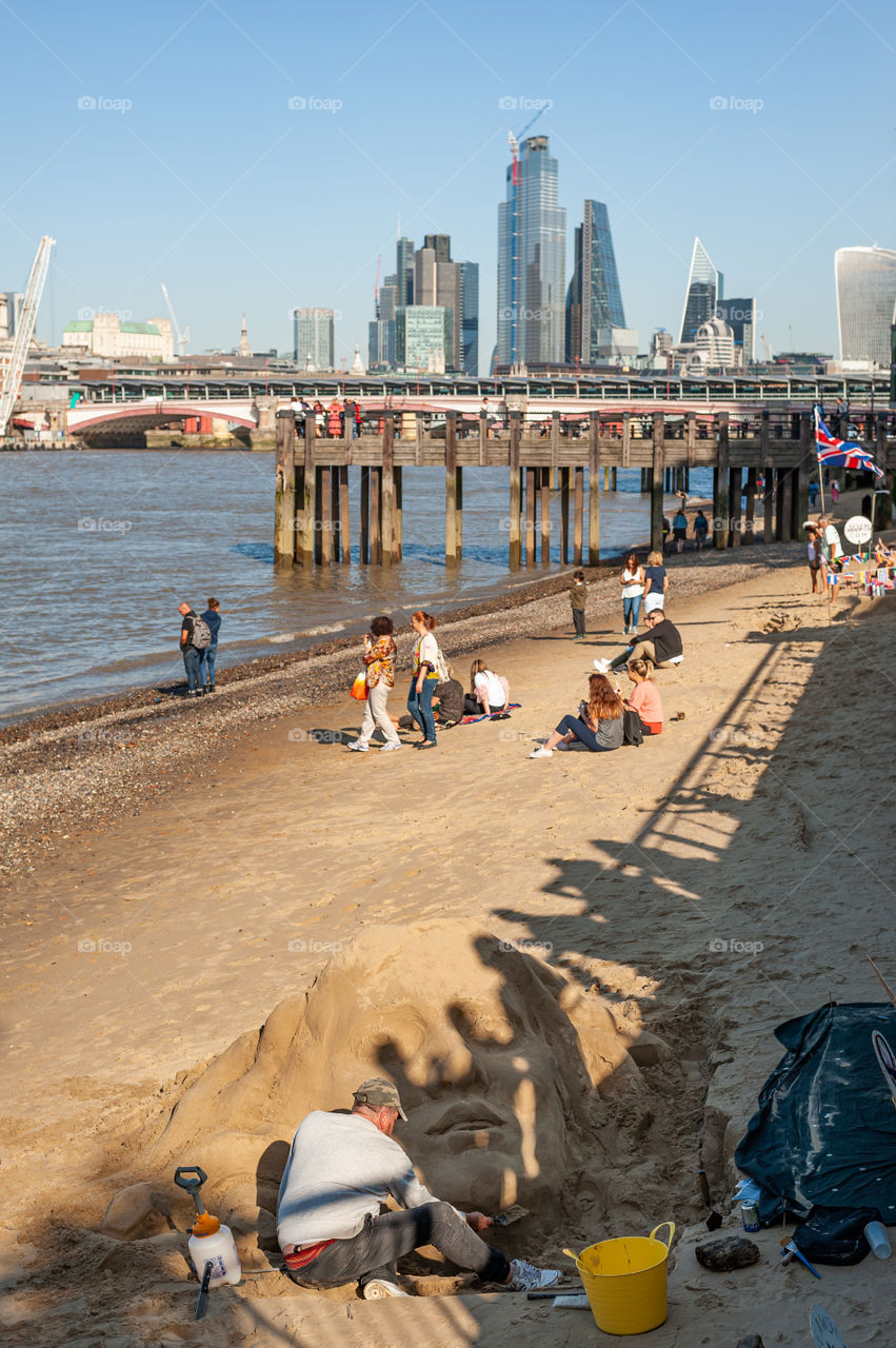 Thames riverbanks. Sand sculpture of Medusa and in distance district of City of London financial hub Square Mile. September 2019. London. UK.