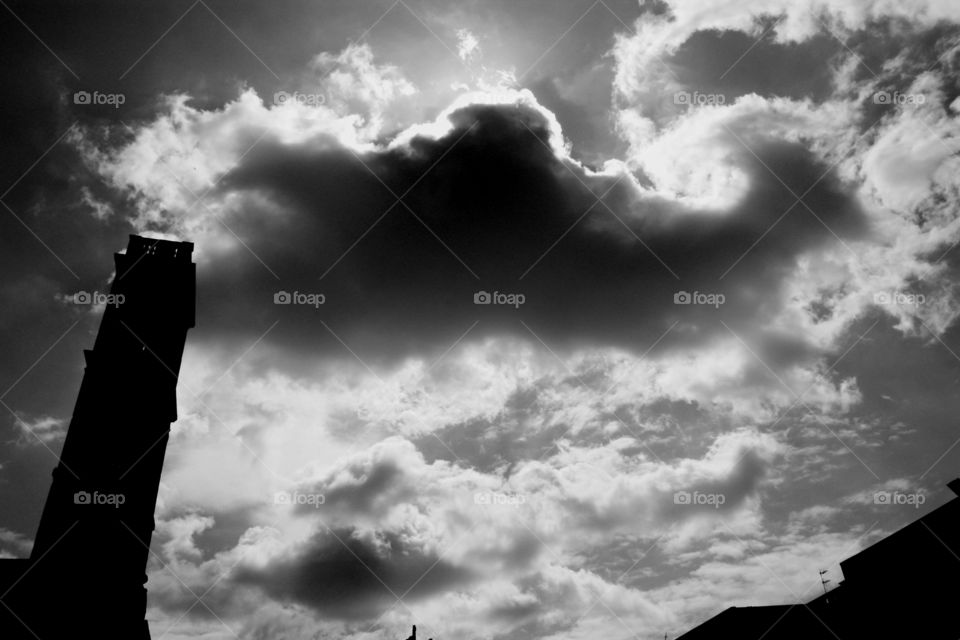 Dramatic black and white capture of a big cloud hovering above a bell tower. Cloudy sky, sinister atmosphere.