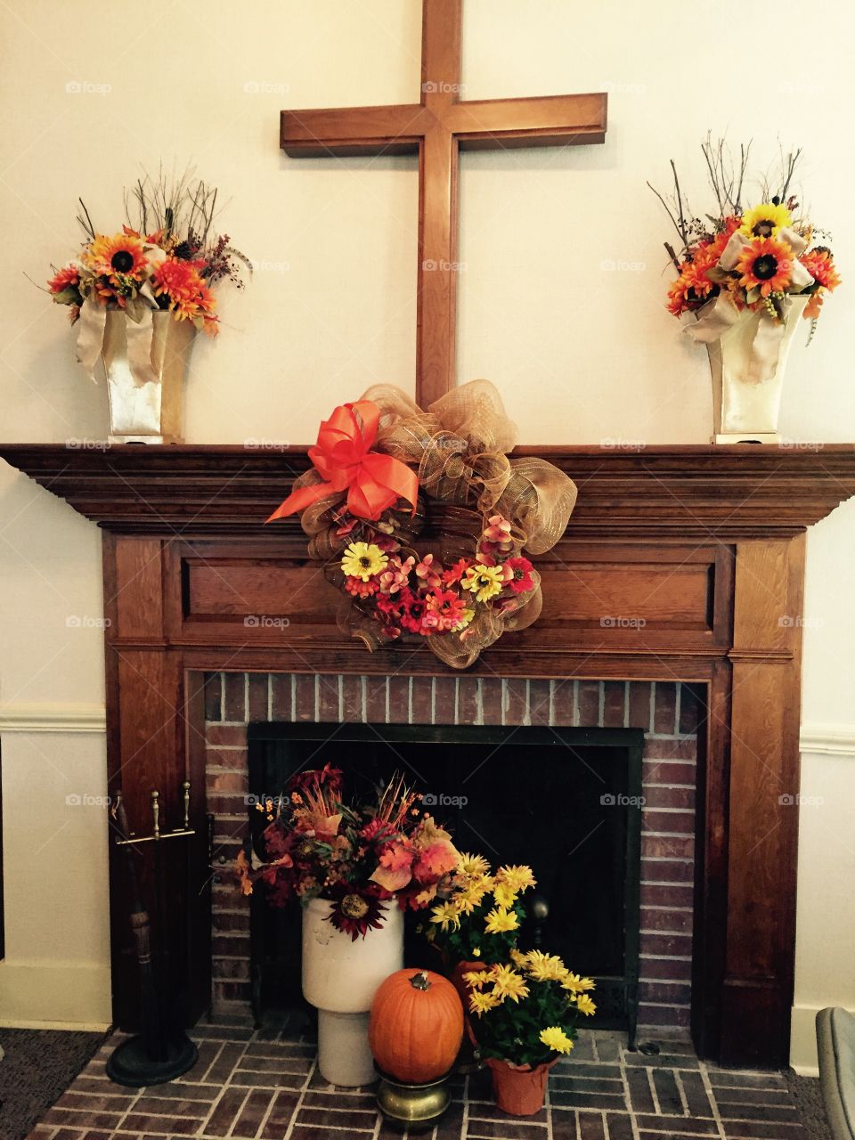 Fall flowers around the fireplace and on the wooden mantel with wooden cross. 