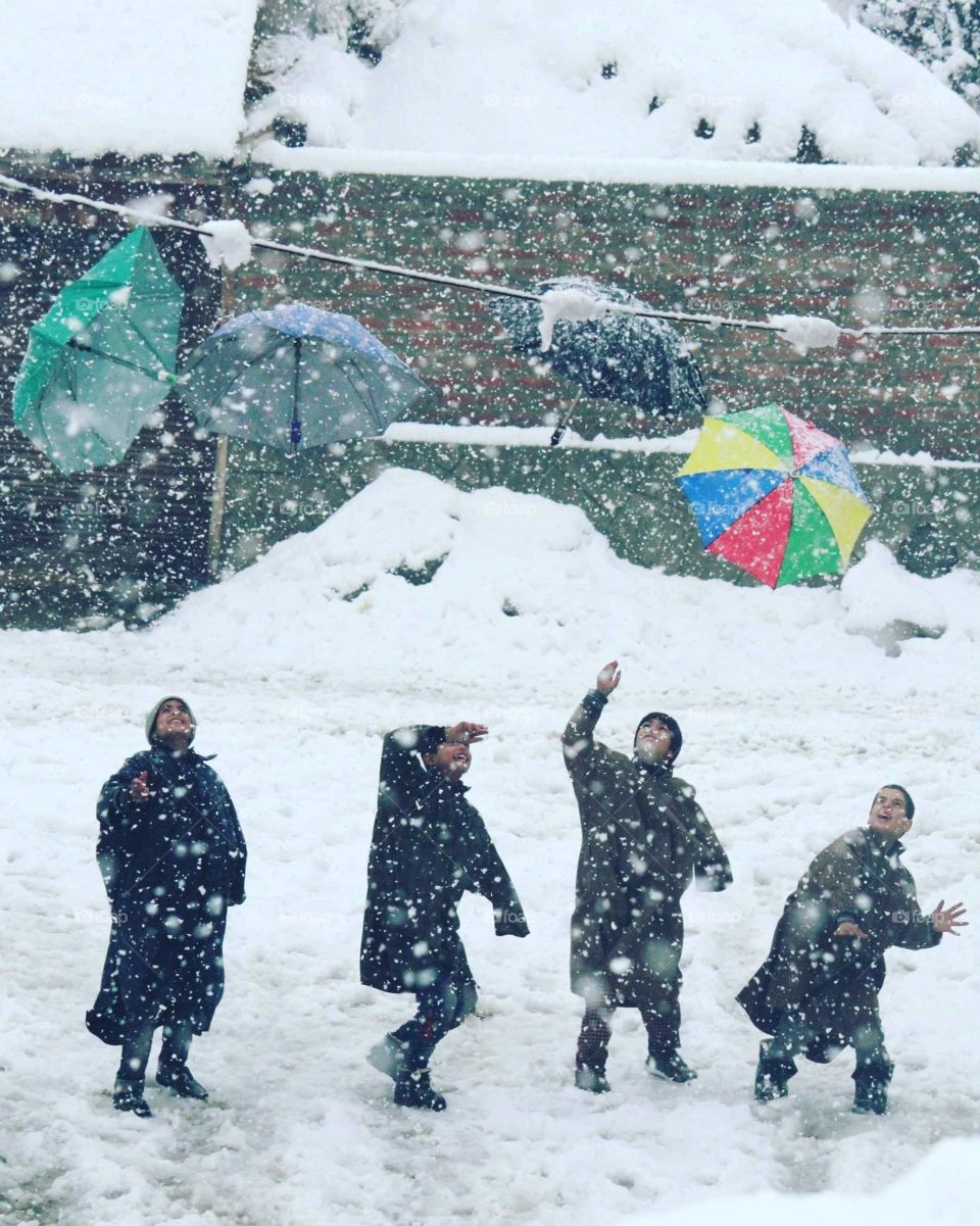 Children enjoy the snowfall by raising up the umbrellas.