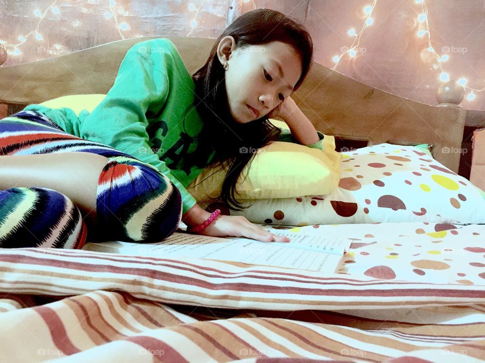 A little girl reading a book in the bedroom