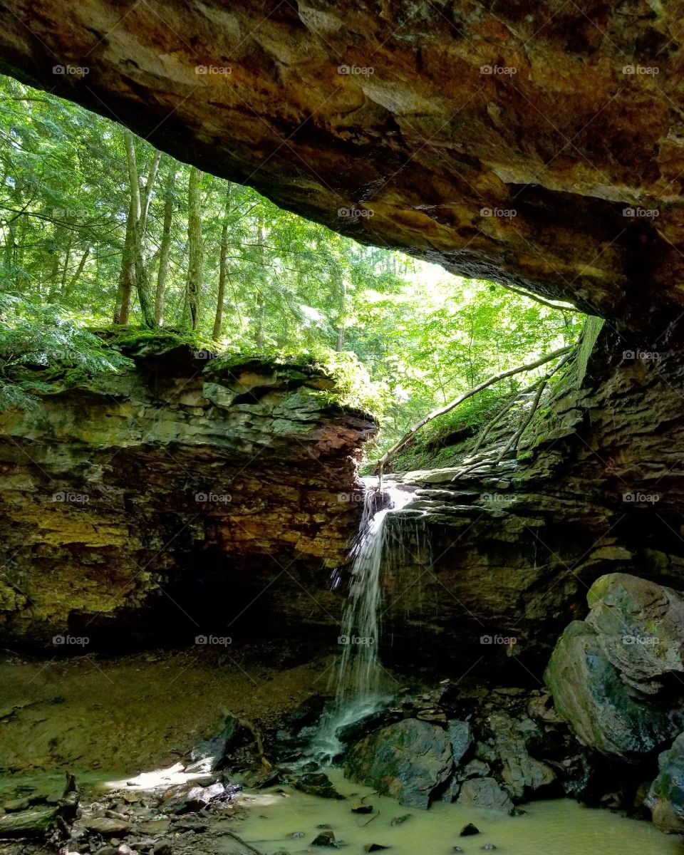 Waterfall pours into pool below from under rock on sunny summer day