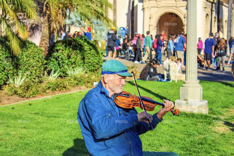 Photo of a man playing a violin in a park to a crowd of people