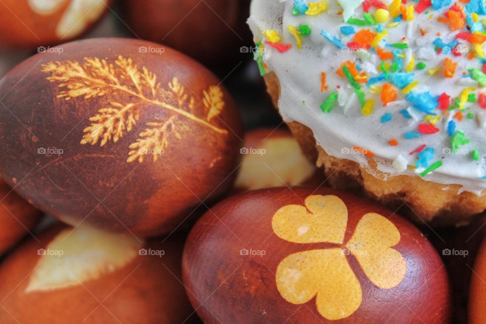 Easter painted eggs with drawings of leaves. the eggs are dyed with onion skins in a uniform natural color. next to it lies a Baked Easter cake with sugar icing and confectionery dressing.