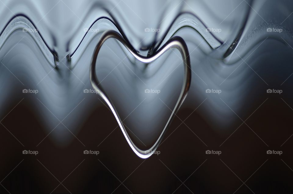 A gold ring reshaped using computer generated imagery is one of a heart with ripples of waves behind it.