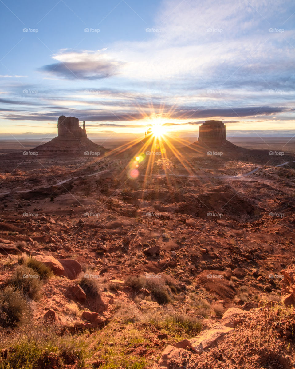 Beautiful sunrise over a desert landscape as the sun rises over ‘the mittens’ of Monument Valley, causing a bright star burst. 