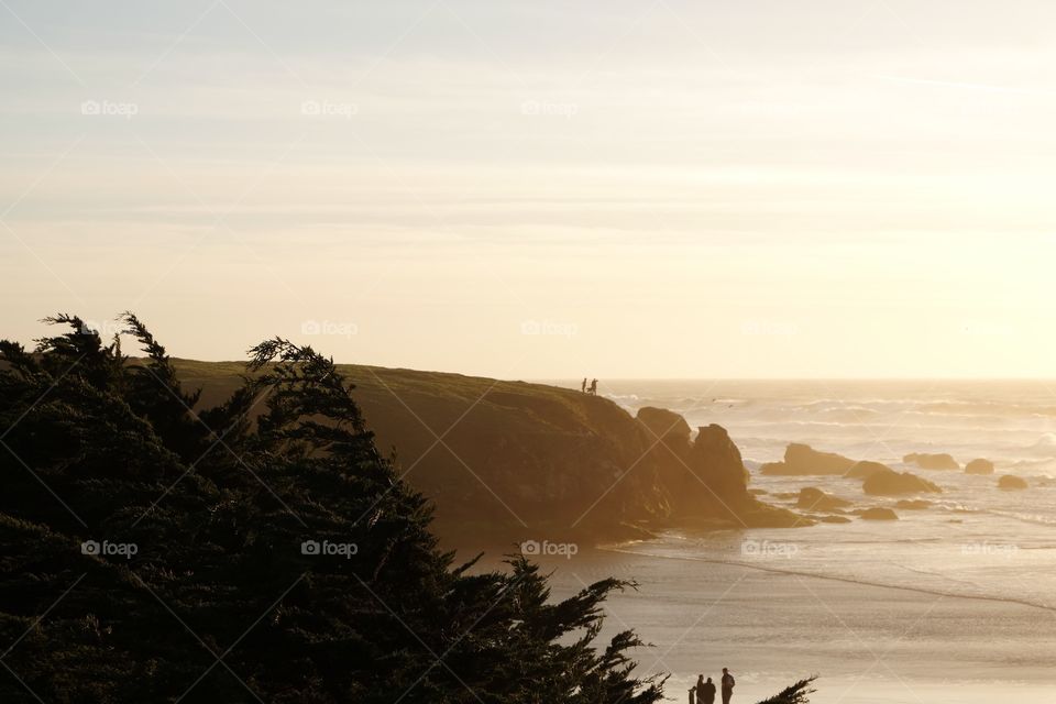 Sun setting off a rocky beach, silhouettes at dusk, people waiting on beach to see sun set