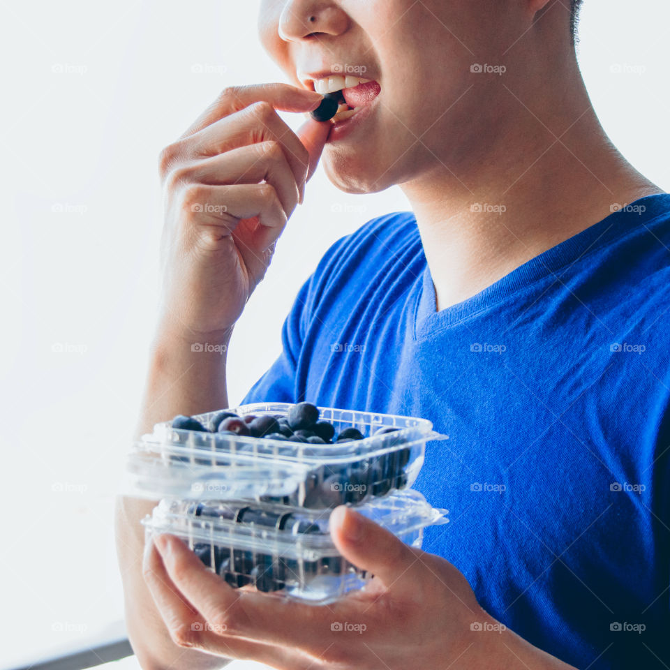 Healthy young man eating blueberries