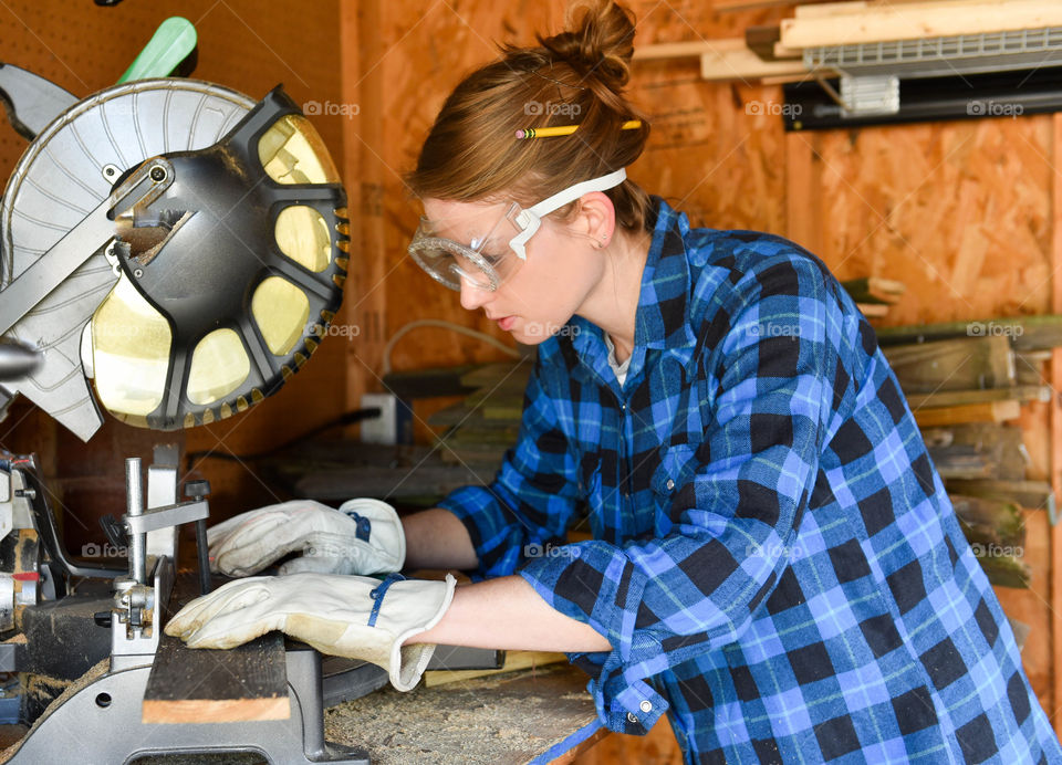 Young millennial woman cutting wood with a miter saw in a shed