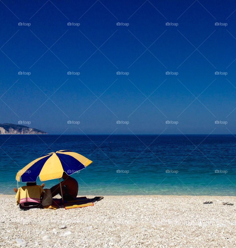 Summertime in Kefalonia ... seeking some shade under a parasol ... love the three blues in this photo and the discarded flip flops just to the right of the image and the casting shadow ... hope you like it too ๐