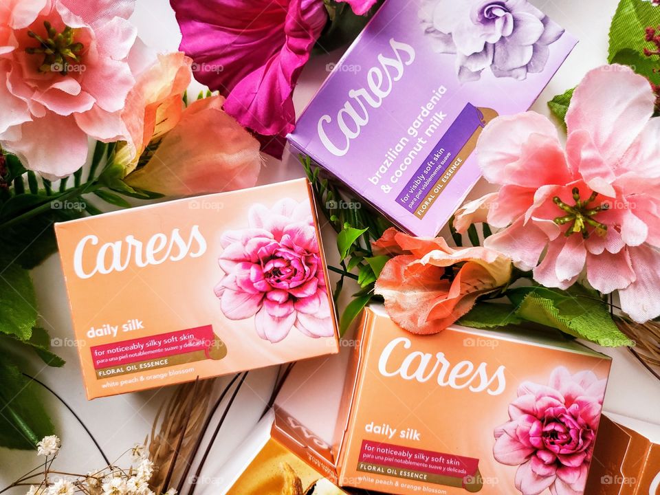 The new look Caress brazilian gardenia & coconut milk and daily silk single pack bar soaps accented by complementary florals on a white background.