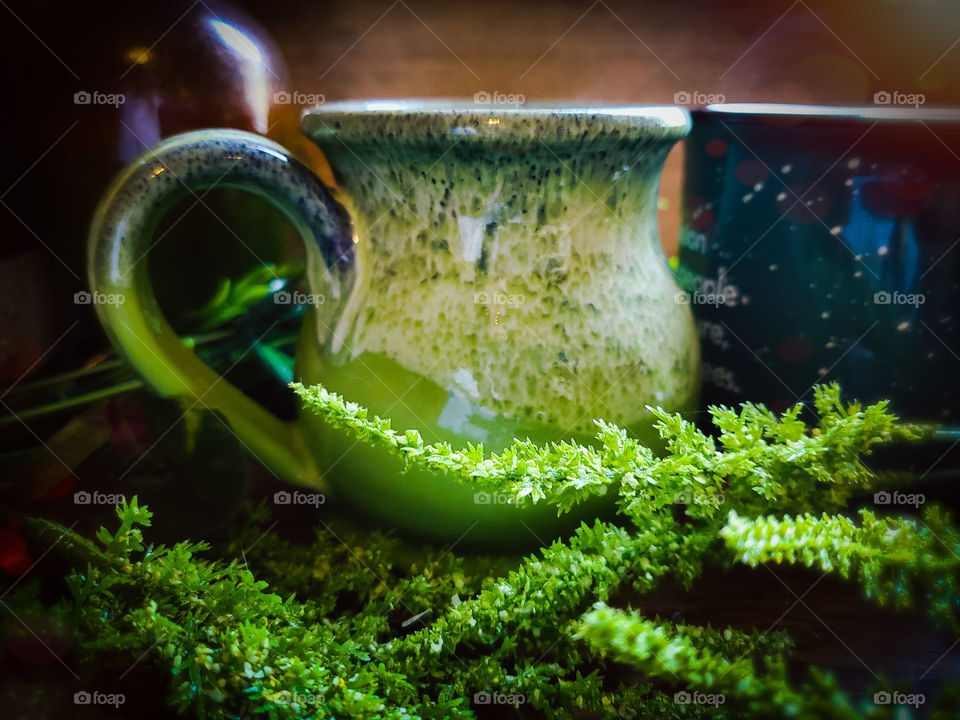 Green clay mug on wood surface wordings by greenery and illuminated by light