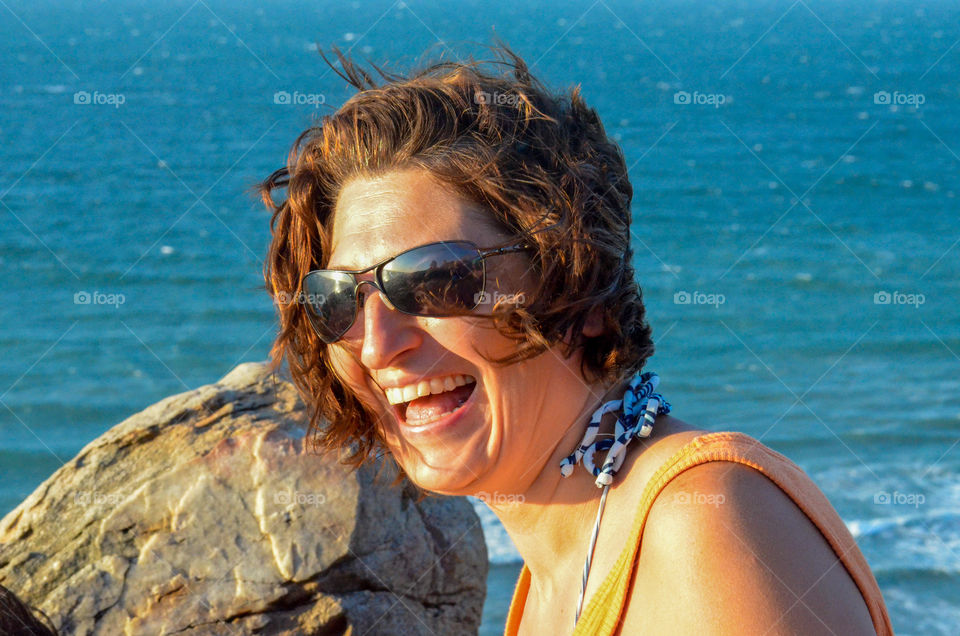 Woman with sunglasses laughing against sky 