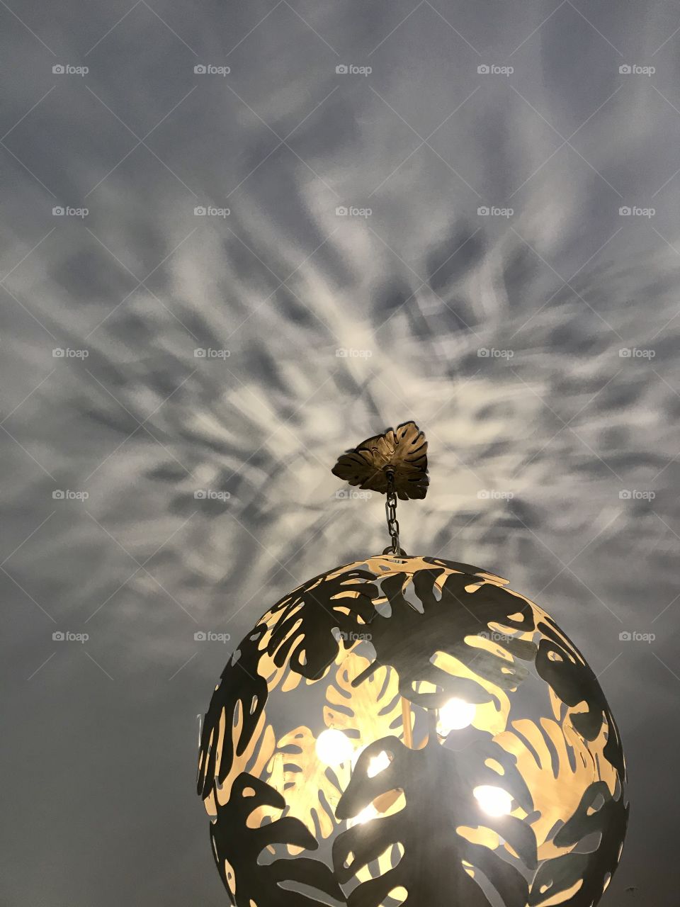 A gold light fixture with sculptured leaves reflecting light onto the ceiling