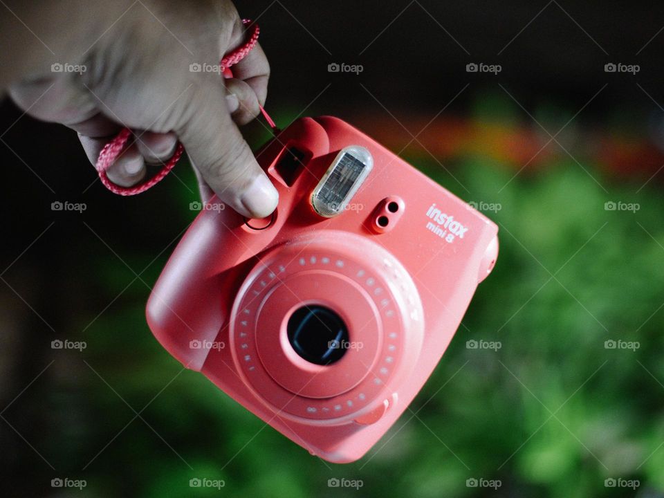 A cropped hand holding an pink instax polaroid camera