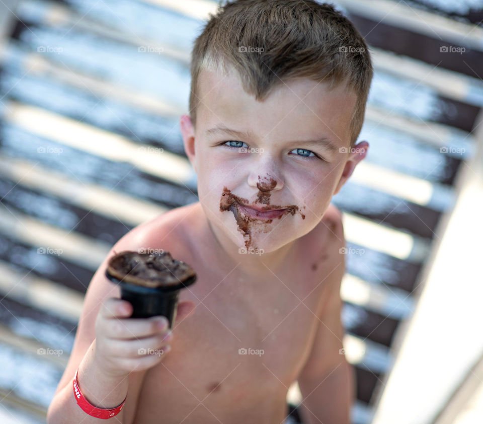 Smiling young boy. Face in chocolate ice cream. Enjoying tasty snack. Tropical vacation. Blue eyed kid