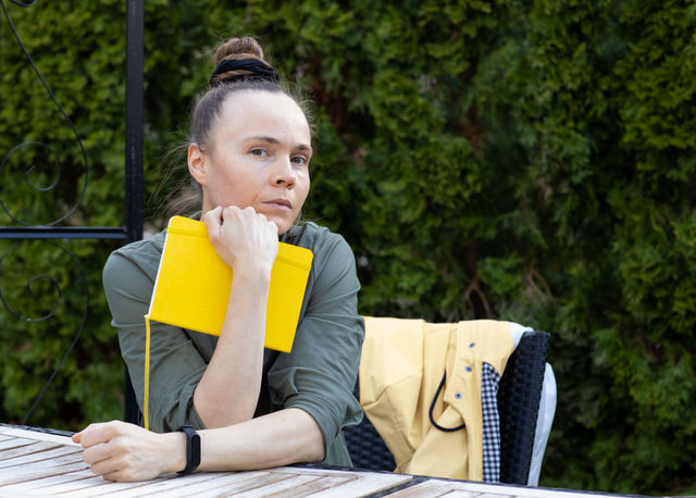 Woman is sitting in the garden with HappySelf Journal. Green background