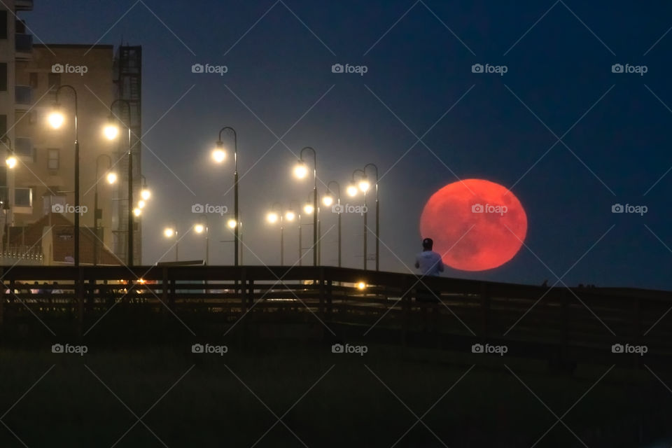 Telephoto compression giving a unique perspective of a huge orange moon rising over a boardwalk. 