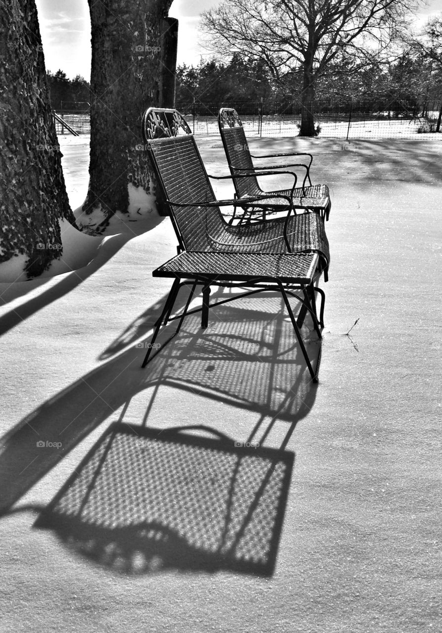 Patio furniture glistening in the winter snow with the sun casting shadows on the snow in black and white