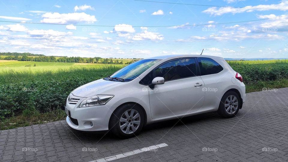 white car on the road against the background of a field and a sunny sky