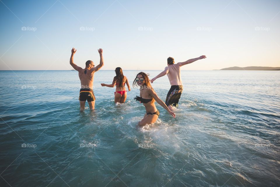 group of friends having fun in the sea during sunset in summertime