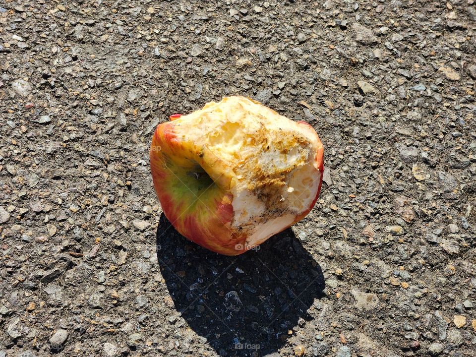 discarded half-eaten apple in a chain store parking lot casting a shadow in the hot weather