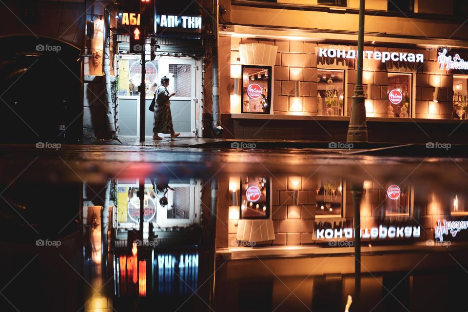 a woman walks down the street looking at a smartphone, in the evening after the rain..