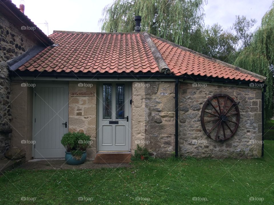 Old, brick wheelhouse with cart wheel on the wall and garden in front with sloping red tiled roof 