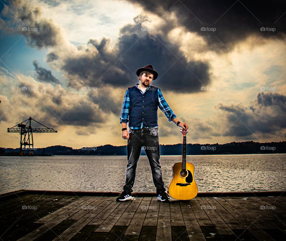 A Man and his guitar.  By the sea into the sunset . Colorful and beautiful skies behandling him