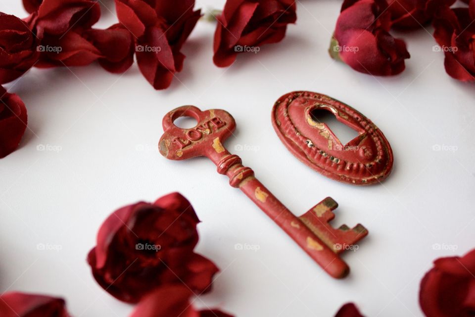 Red, metal, vintage key and keyhole with red, silk rose buds on white marble surface