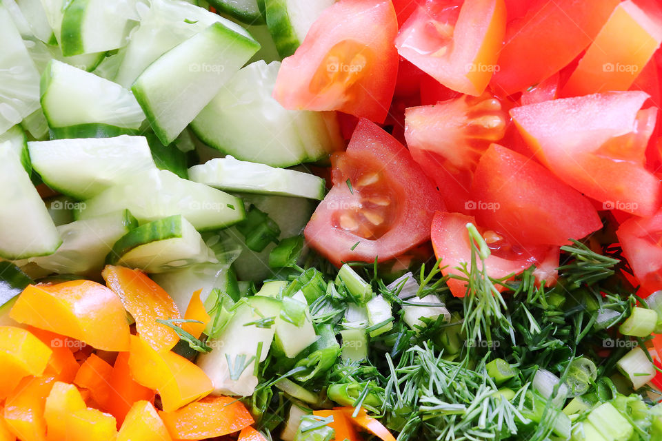 A plate of salad from chopped vegetables. Green cucumber, red-orange sweet pepper, red tomato, green onions and dill.